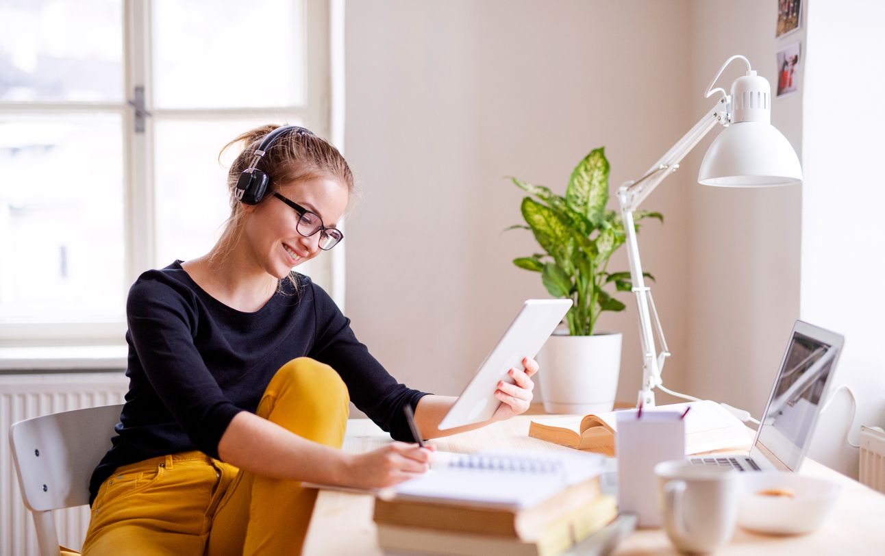 A young female student sitting at the table, using tablet when studying.