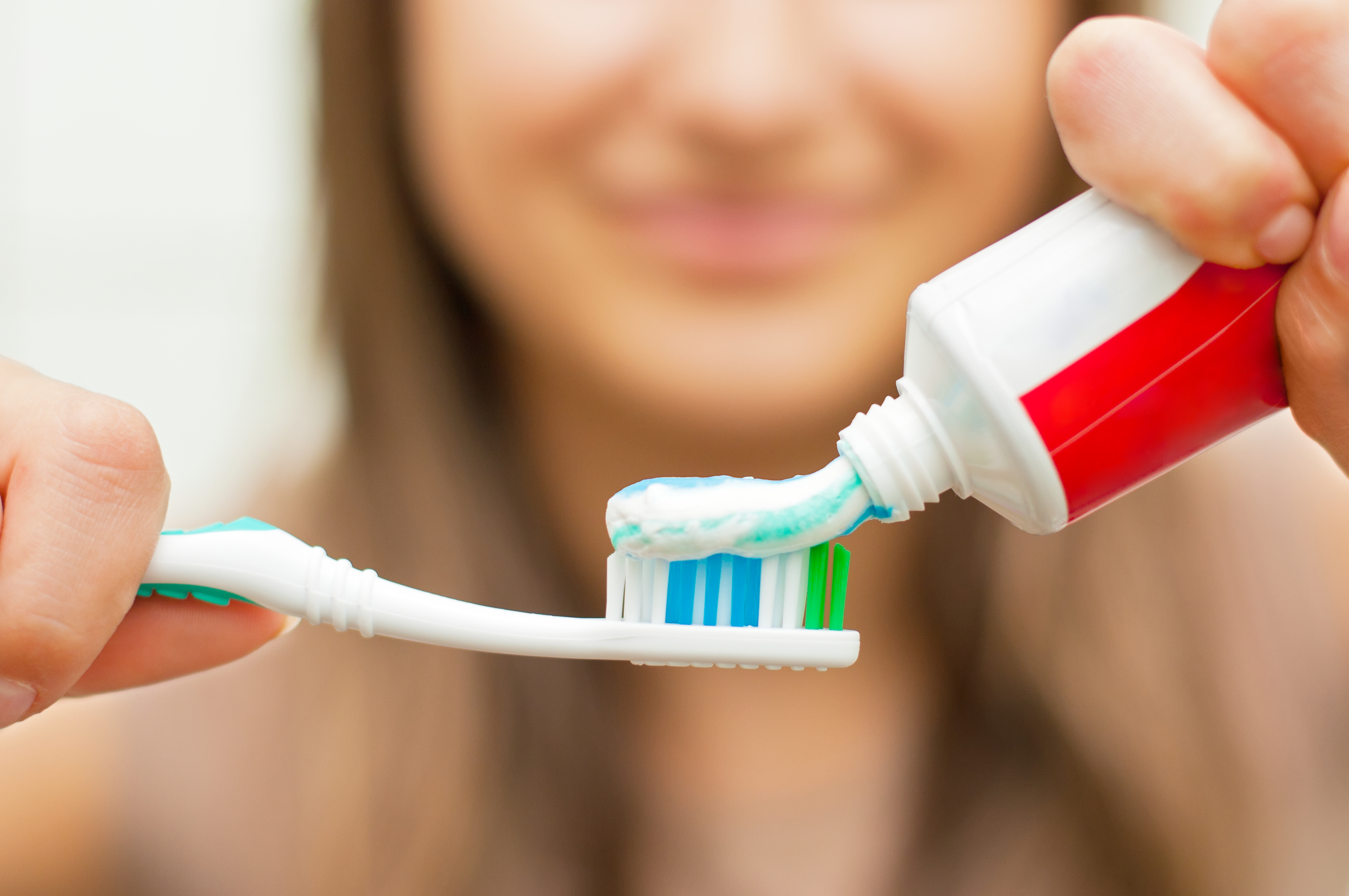 Young woman holding a toothbrush and placing toothpaste on it.