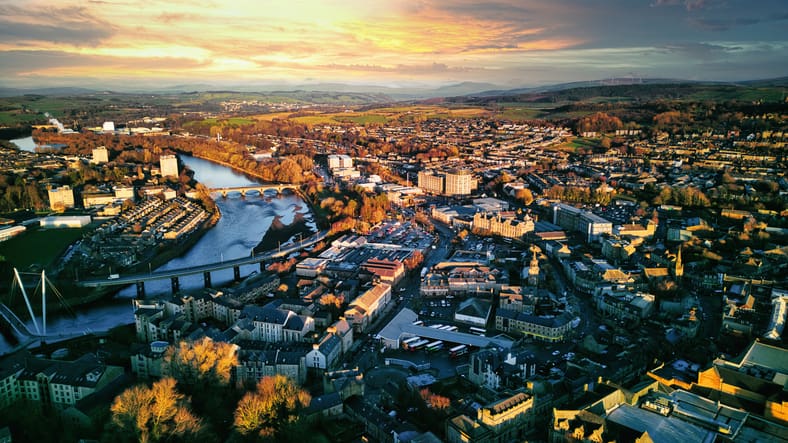 Aerial view of a city Lancaster at sunset with warm lighting, showcasing the urban landscape, buildings, and a river flowing through the center.